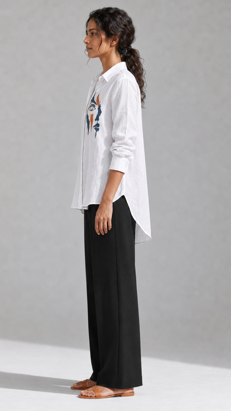 White shirt showing the hand-embroidered abstract face motif at the left chest, side view
